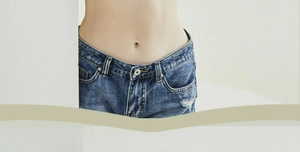 Detail of dark blue denim jeans showing the metallic button waist and pocket distressing