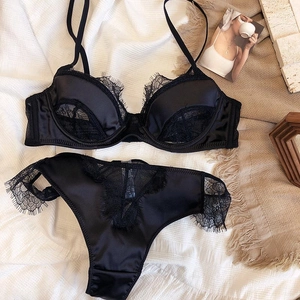 Flat lay of black eyelash lace lingerie set with silk texture on a white background