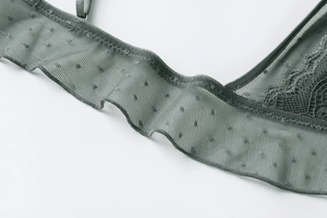 Dettaglio ravvicinato del reggiseno in pizzo grigio-verde con rete a pois e ricami