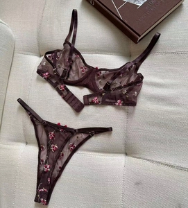 Flat lay of sheer burgundy lace lingerie set with pink floral embroidery on beige fabric