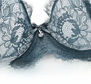 Detail of blue-green lace bra with satin bow, rhinestone pendant, and floral embroidery
