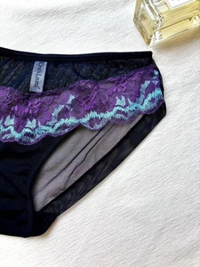 Détail d'une culotte en résille avec broderie en dentelle bicolore et étiquette tissée