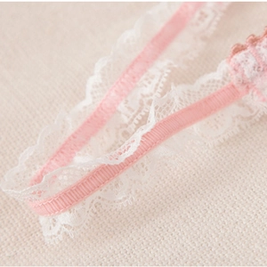 Détail d'une bretelle en satin rose avec broderie florale délicate en dentelle blanche