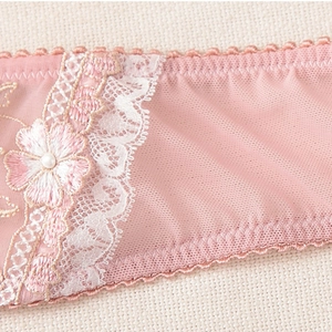Détail macro de dentelle rose avec broderie florale blanche et perle décorative