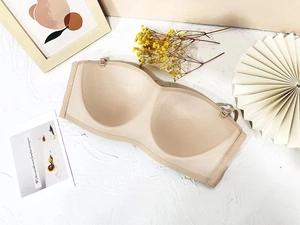 Flat lay of seamless strapless nude bra on white textured surface with elegant props