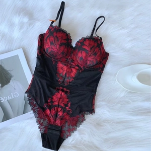 Detailed view of red and black floral lace embroidery on a mesh bodysuit on plush background