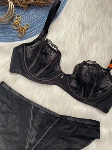Close-up of black lace lingerie set with metal pendant detail on soft white faux fur