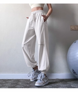 Detail view of cream-white drawstring joggers with decorative metal buckles and elastic cuffs