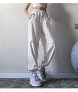 Detail of high-waist drawstring joggers in beige showing textured fabric and side buttons