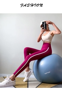 Detail view of high-waisted rose red yoga pants with side stripes on a gym ball