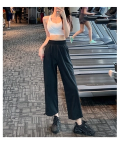 Detail of high-waist black quick-dry track pants and white sports bra in gym setting