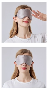 Silver silk sleep mask with black elastic straps worn by a model on a grey background