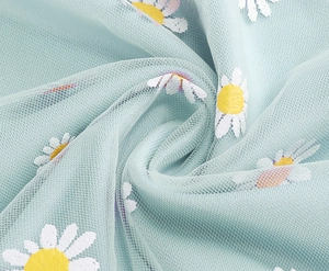 Detail of light blue mesh fabric featuring white daisy embroidery and floral textures