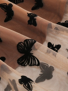 Dettaglio ravvicinato del tessuto in tulle beige con farfalle nere in rilievo e pieghe