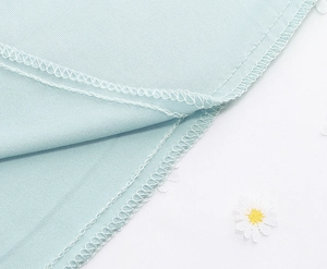 Detail of mint blue fabric showing double-stitched hem and white daisy embroidery on mesh