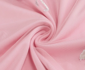 Close-up of pink mesh fabric featuring delicate white embroidery and soft texture