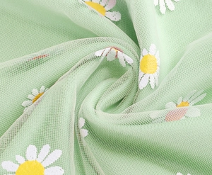 Close-up of light green mesh tulle fabric with white daisy floral embroidery detail