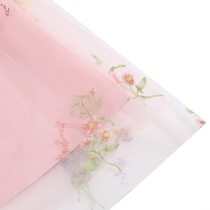 Dettaglio del ricamo floreale e scritte artistiche su tessuto in rete rosa e bianco