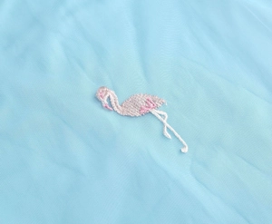 Detailed view of high-quality flamingo embroidery on light blue fabric texture