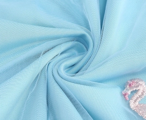 Detail of pink flamingo embroidery on light blue mesh tulle fabric with elegant texture