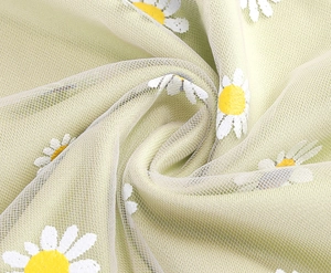 Detailed macro view of mint green mesh fabric featuring vibrant white daisy embroidery