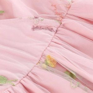 Dettaglio di un abito in tulle rosa con ricami di margherite e scritte in corsivo