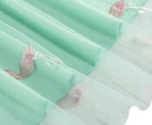 Close-up of mint green tulle skirt featuring delicate pink flamingo embroidery and wavy hem