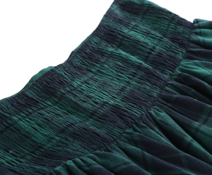 Detailed macro view showing the elastic smocking waist and green plaid fabric of the skirt