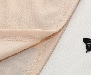 Dettaglio delle cuciture sottili sulla gonna a pieghe beige con ricamo a farfalla