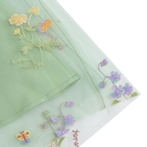 Dettaglio ravvicinato di ricami floreali e farfalle multicolori su tulle verde