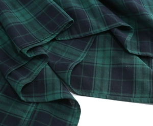 Detailed close-up of green and black plaid fabric with neat hem stitching on the skirt