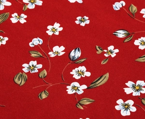 Close-up of red floral fabric with white petals and yellow centers on a cotton texture