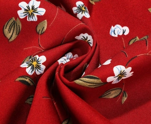 Macro shot of red floral fabric detail showing white blossoms and green leaf texture