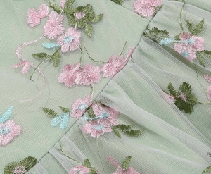 Detail of light green mesh fabric featuring delicate floral embroidery on a dress