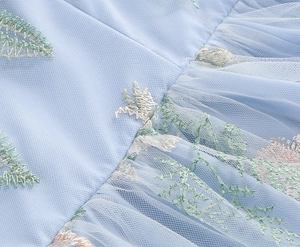 Detailed close-up of light blue mesh fabric with delicate floral embroidery on long dress