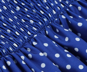Détail d'une robe bleu marine à pois avec bustier smocké élastique et ourlet à volants