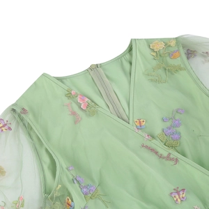 Dettaglio dello scollo a V con delicati ricami floreali e farfalle su un abito verde chiaro