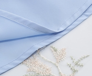 Detail of light blue fabric with intricate floral embroidery on white mesh layering