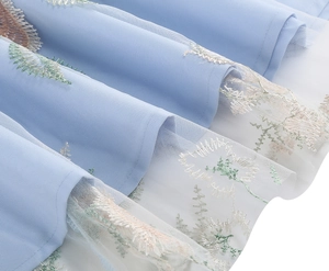 Detailed close-up of delicate multi-color embroidery on a light blue mesh tulle dress