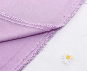 Detailed macro view of white overlock stitching on purple mesh fabric with daisy embroidery