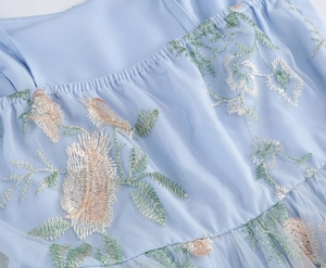 Detail of light blue mesh dress featuring multi-color floral embroidery and elastic pleats