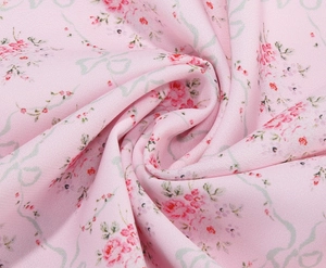 Detailed macro shot of pink embroidered fabric with small red flowers and green ribbons