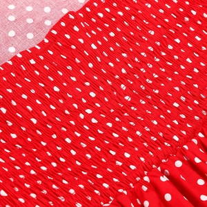 Close-up of red polka dot dress fabric featuring detailed elastic smocking texture