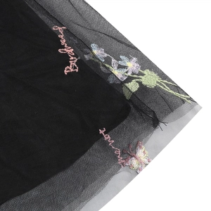 Dettaglio di ricamo floreale e scritte rosa su tessuto a rete nero per un vestito