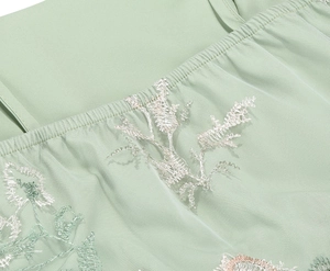 Detailed view of floral embroidery on light green tulle fabric with gathered elastic hem