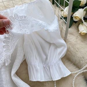 Dettaglio del ricamo in pizzo e dei polsini elastici su una camicia bianca con spalle scoperte
