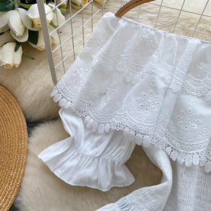 Dettaglio del top bianco a spalle scoperte con ricami floreali e maniche a balze
