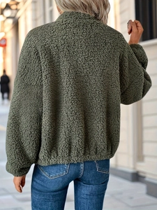 Rear view of a dark green faux shearling jacket with casual blue jeans in a street setting