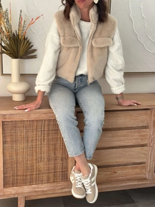 Detail of beige faux fur vest with zipper closure and front pocket on female model