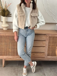 Detail showing beige faux fur vest styled with a white sweater and blue denim jeans